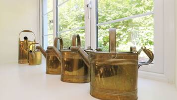 Four brass watering cans on a windowsill with a view of trees outside.