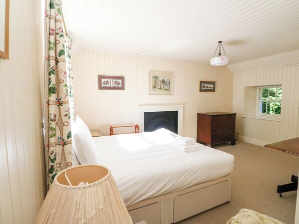 A bedroom with a bed, a dresser, a lamp, a fireplace, and a window. - Gardeners Cottage (Perth)