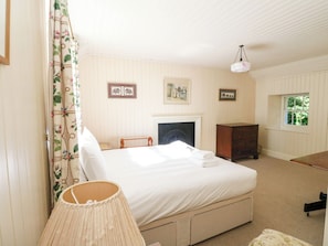 A bedroom with a bed, a dresser, a lamp, a fireplace, and a window.