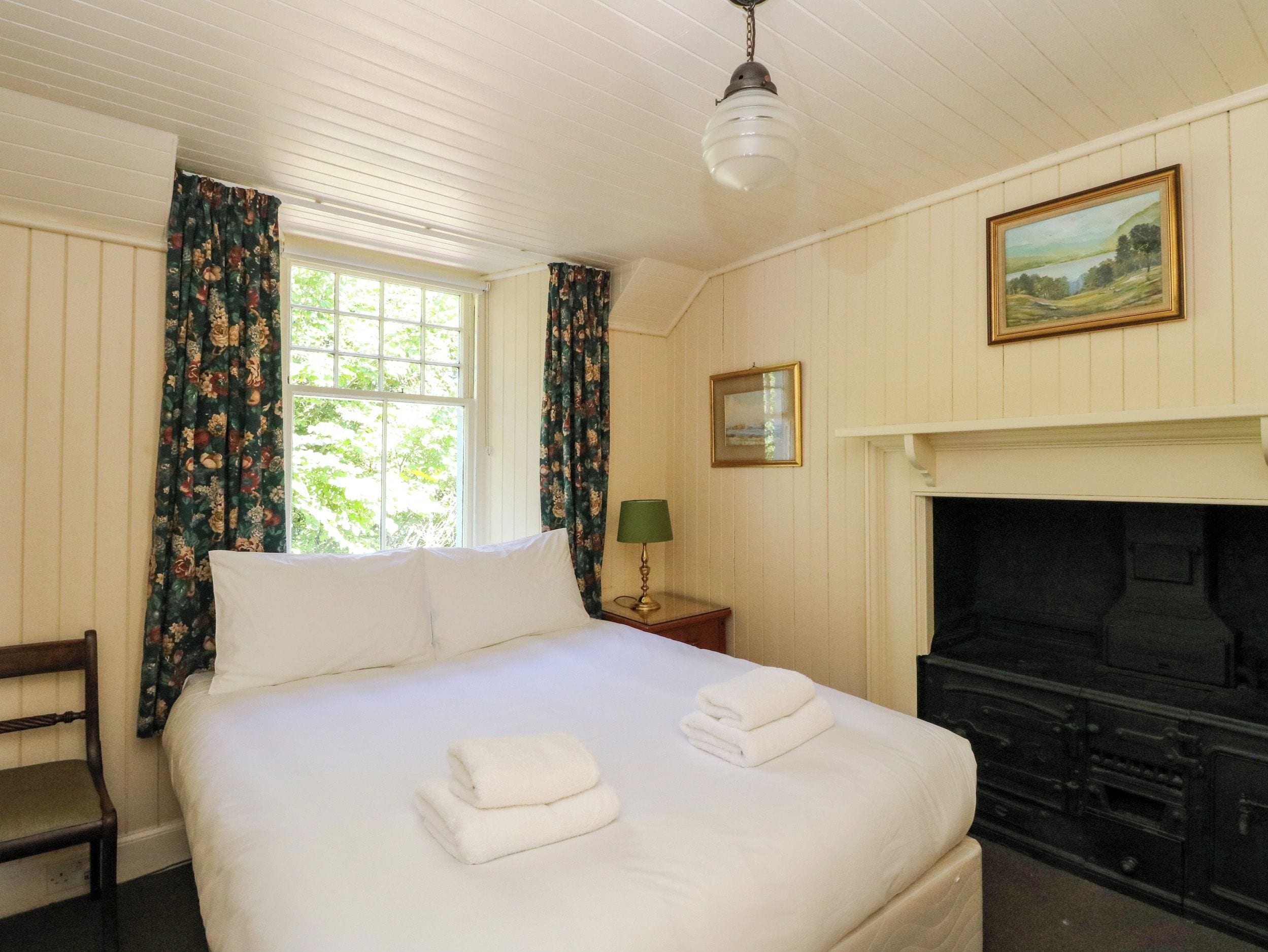 A hotel room with a bed, a fireplace, a painting, and a window with curtains.