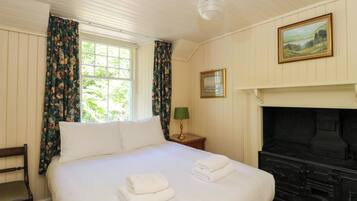 A hotel room with a bed, a fireplace, a painting, and a window with curtains.
