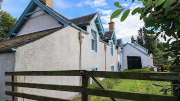 Una casa tradicional con fachada blanca y detalles azules, un portón de madera en primer plano y un jardín con césped.