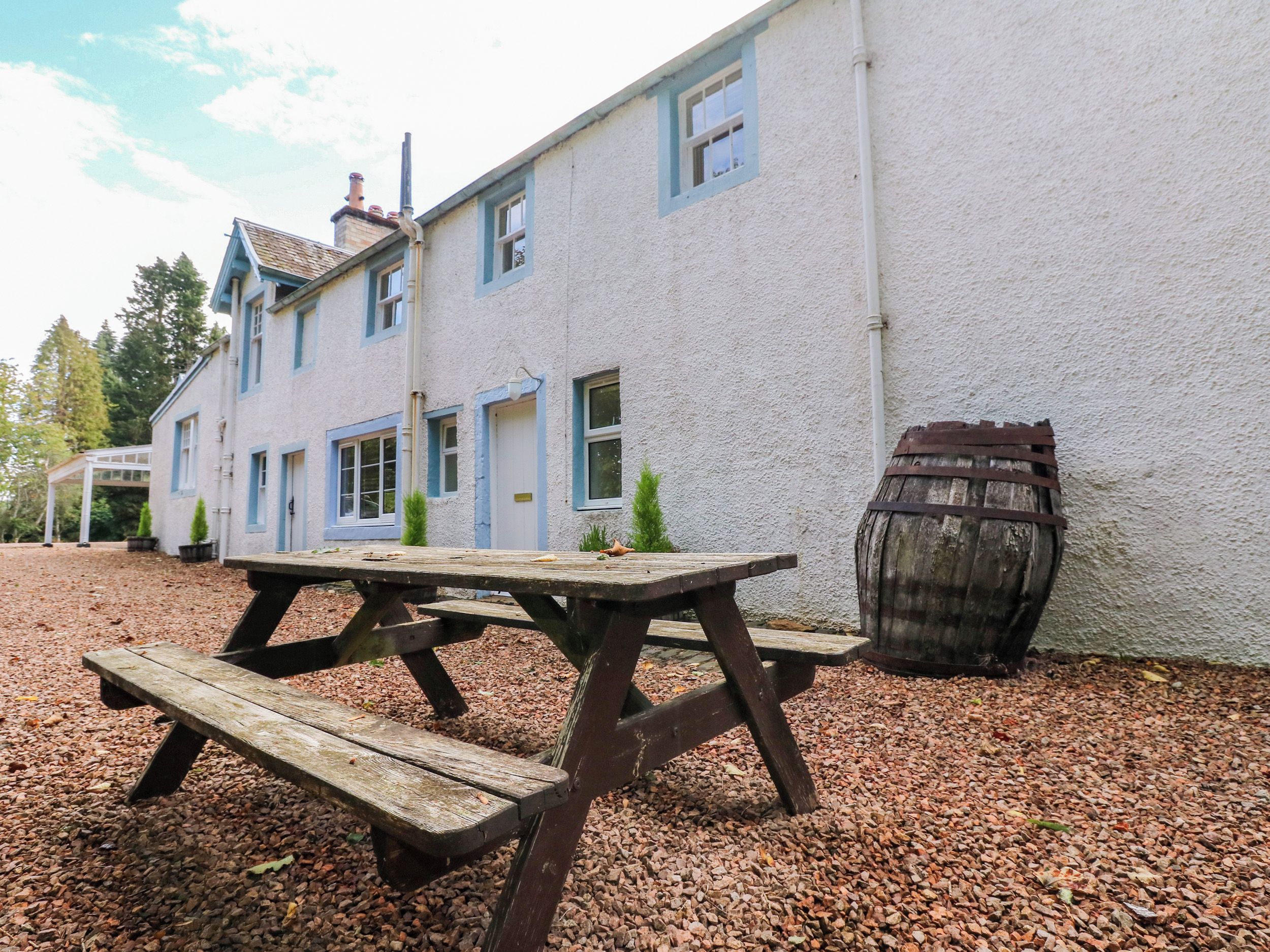A picnic table outside a building with a barrel.