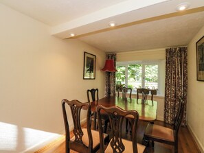 A dining room with a large wooden table and chairs, a red lamp, and a window with curtains. - Gardeners Cottage (Perth)