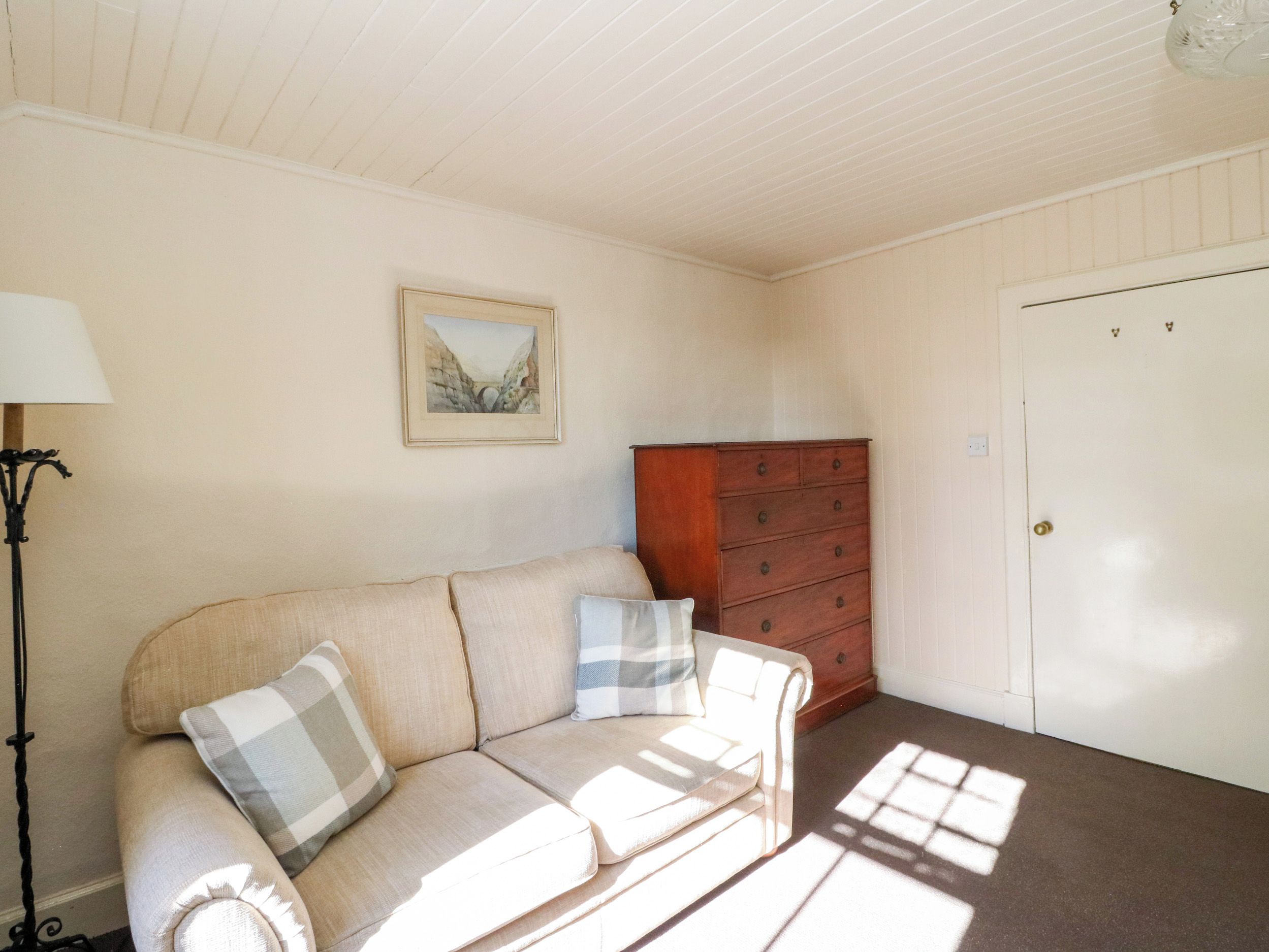 Una habitación con un sofá color beige, un aparador de madera, un cuadro enmarcado en la pared y una puerta.