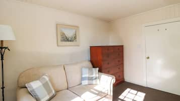 Una habitación con un sofá color beige, un aparador de madera, un cuadro enmarcado en la pared y una puerta.