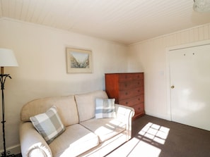 Une pièce avec un canapé beige, une commode en bois, un tableau encadré au mur et une porte.