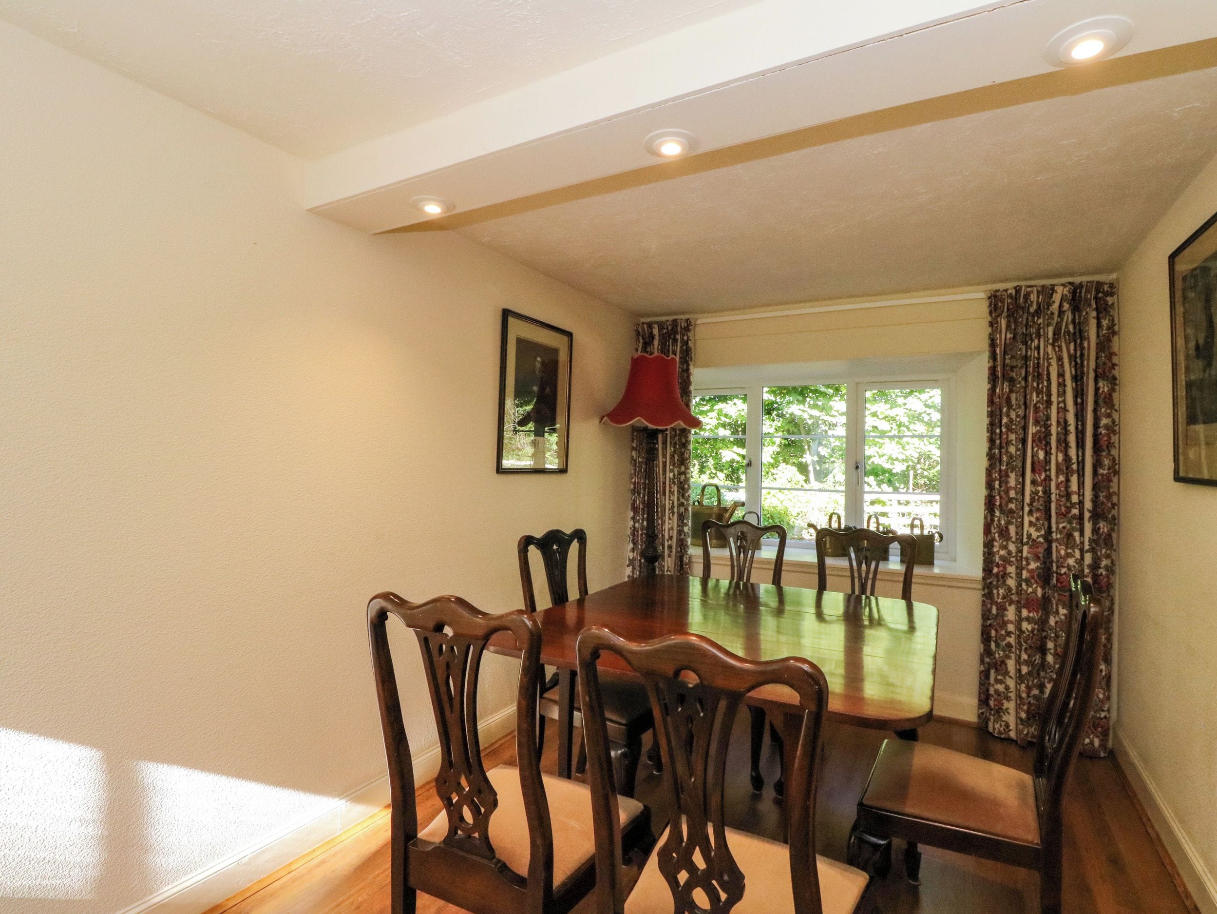 Une salle à manger avec une grande table et des chaises en bois, une lampe rouge et une fenêtre avec des rideaux.