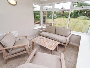 Ein Wintergarten mit einer Couch, Sesseln und einem Tisch.