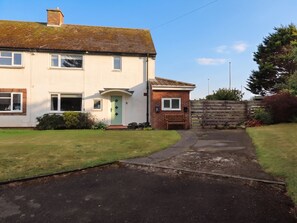 A two-story house with a front garden, a paved driveway, and a wooden fence. - Bari House (Seahouses)