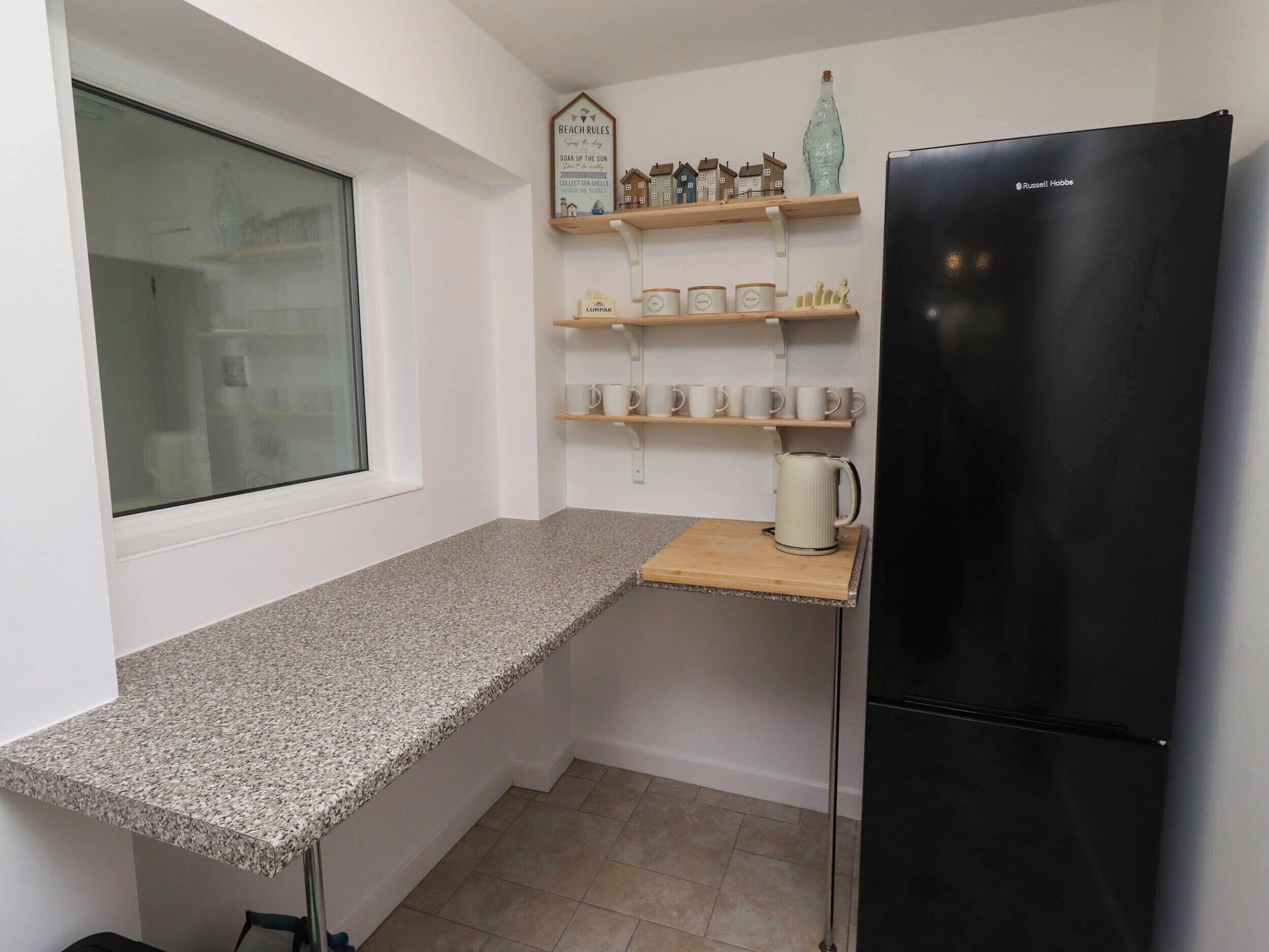 A kitchen with a granite countertop, a black refrigerator, and shelves with kitchenware.