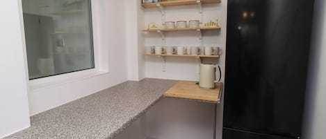 A kitchen with a granite countertop, a black refrigerator, and shelves with kitchenware.