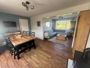 Ein Essbereich mit Holztisch und Stühlen, ein Wohnzimmer mit Sofa und Fenster sowie eine Küchenzeile mit Herd.