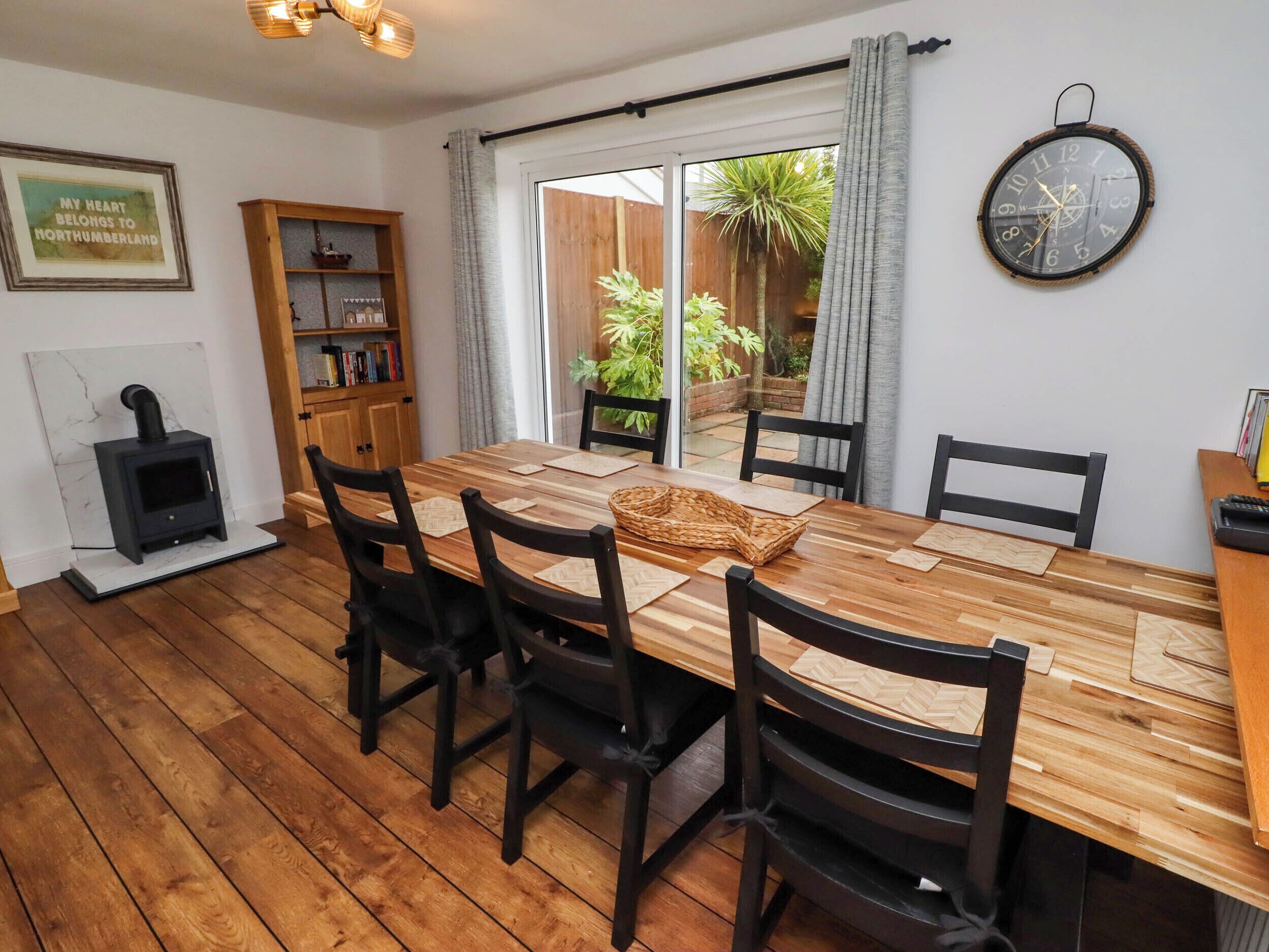 A dining area with a wooden table, black chairs, a woven basket, and a clock on the wall.