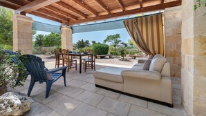 An outdoor patio with a wooden pergola, stone walls, a table with chairs, and a beige sofa. - Il Trullo del Colonnello – Exclusive Historic Stay Near the Sea (Torre Lapillo)