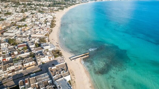 An aerial view of a coastal town with a beach, buildings, and a pier extending into the sea. - Il Trullo del Colonnello – Exclusive Historic Stay Near the Sea (Torre Lapillo)