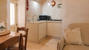A compact kitchen with a dining area, a stove, a microwave, and a hanging pot. - Il Trullo del Colonnello – Exclusive Historic Stay Near the Sea (Torre Lapillo)