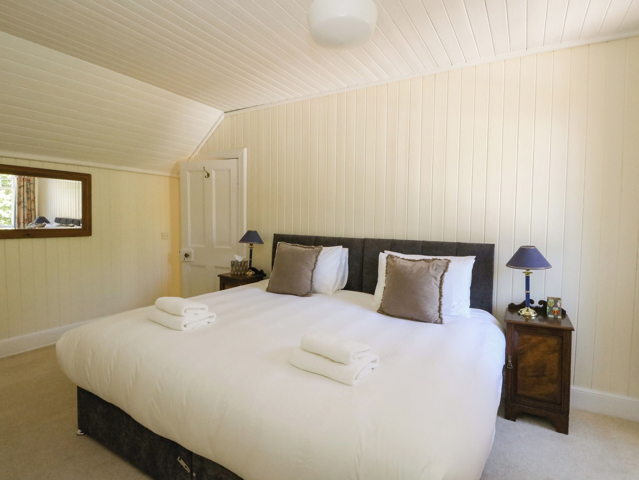 A bedroom with a large bed, two bedside tables, a mirror, and a door.