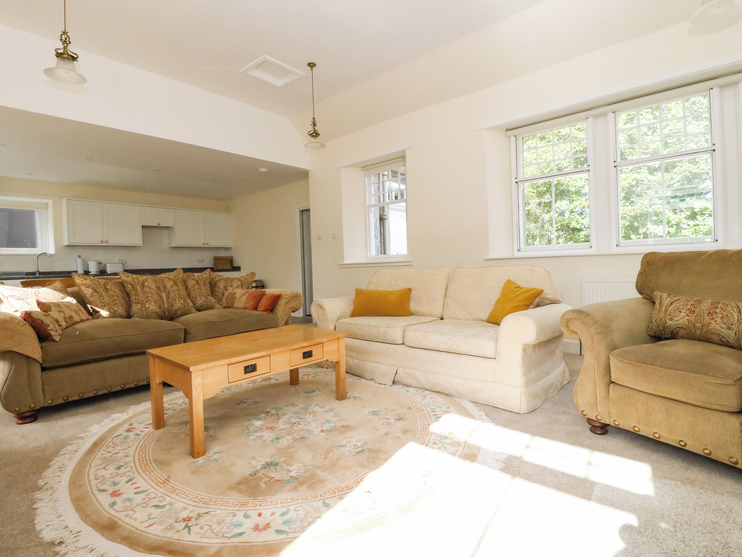 A living room with a sofa set, a coffee table, and a rug. There is a window with a view of trees.