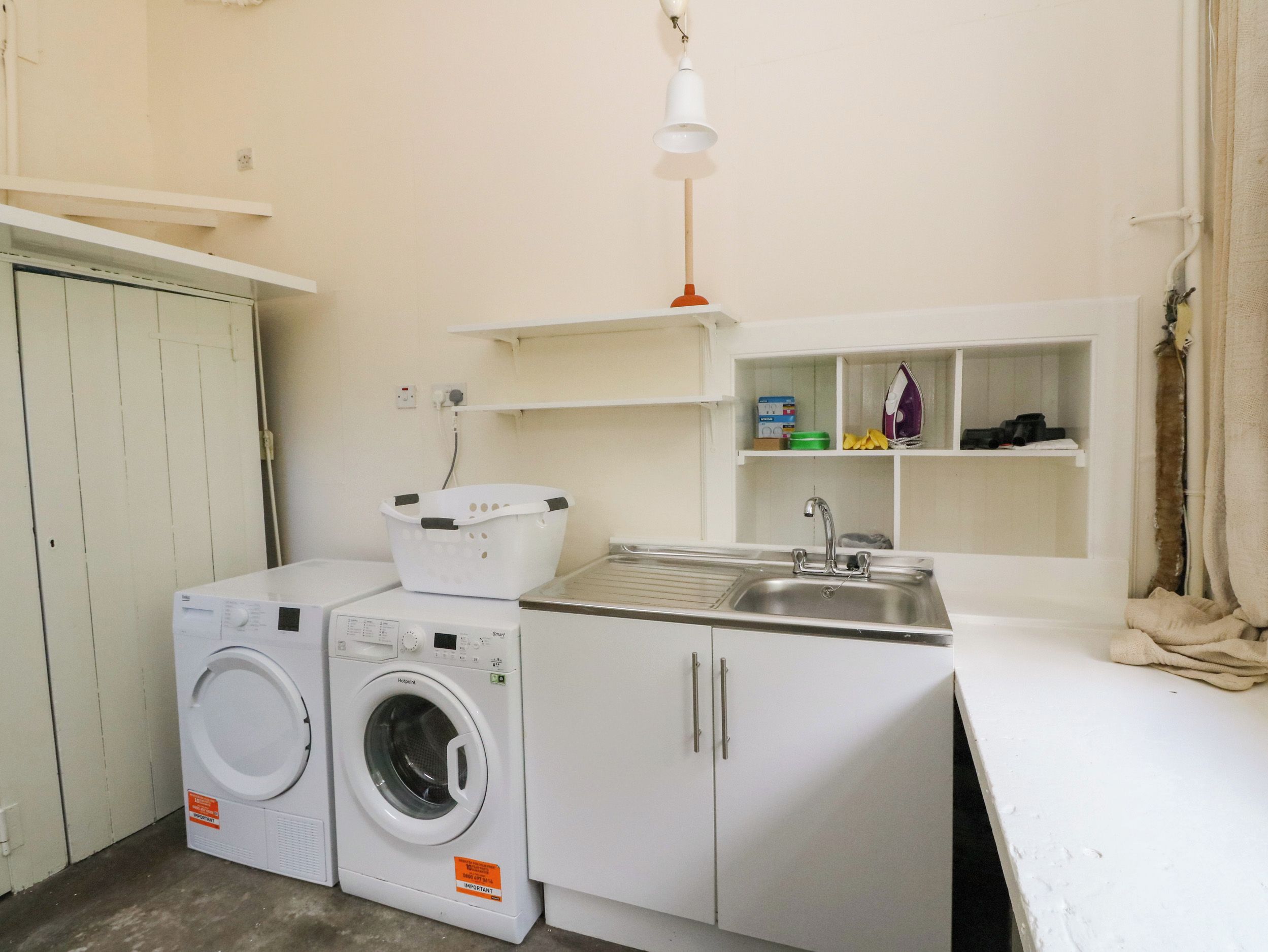 Un área de lavandería compacta con lavadora, secadora, lavabo y estantes de almacenamiento.