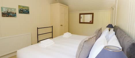A hotel room with a bed, a bedside table, a lamp, a radiator, and two paintings on the wall.