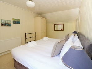A hotel room with a bed, a bedside table, a lamp, a radiator, and two paintings on the wall.