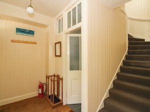 Un escalier menant à un deuxième étage, un extincteur, un porte-manteau, une porte avec un panneau en verre dépoli et un luminaire fixé au mur.
