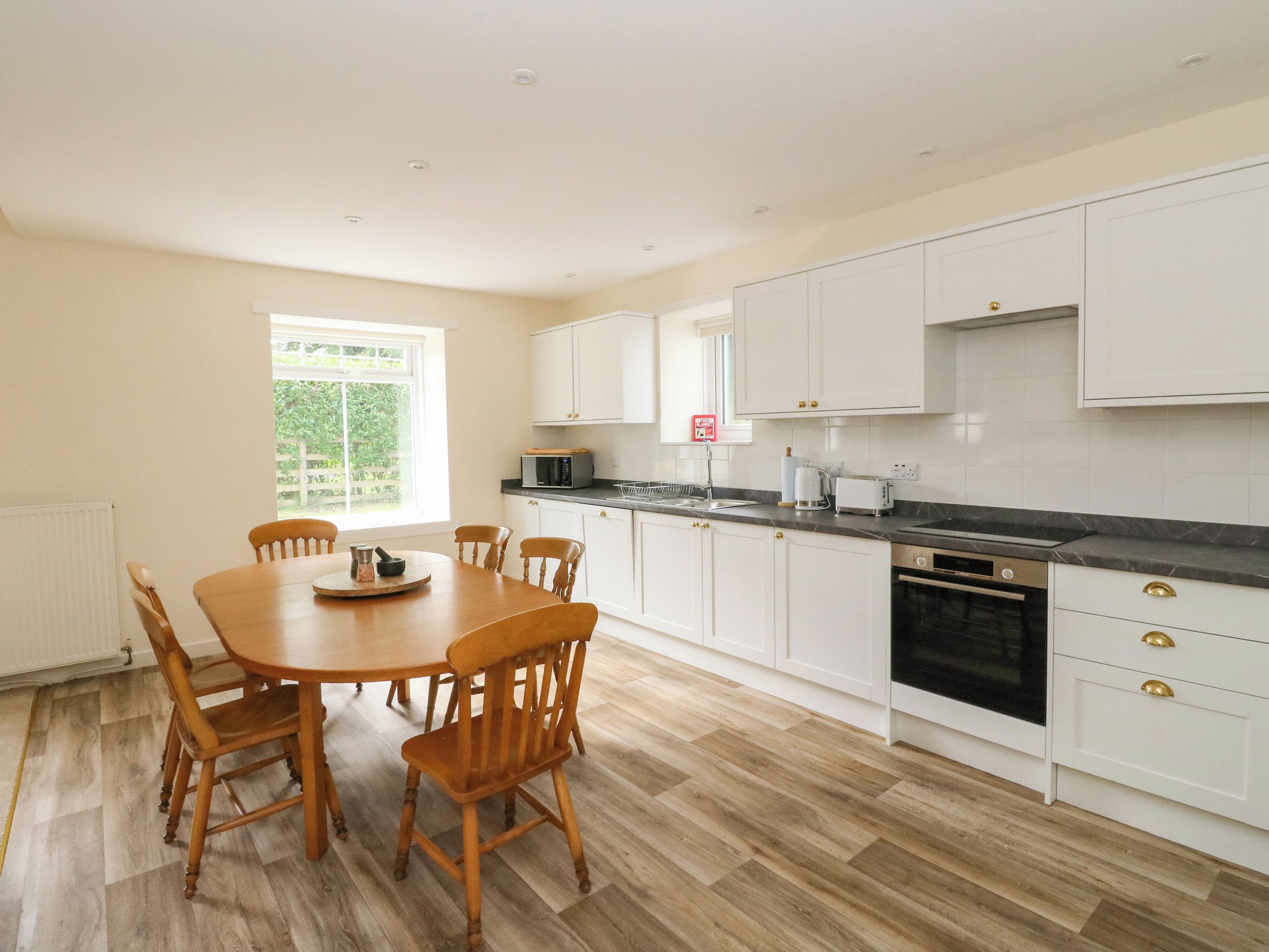 A modern kitchen with white cabinets, a black countertop, and a dining table with wooden chairs.
