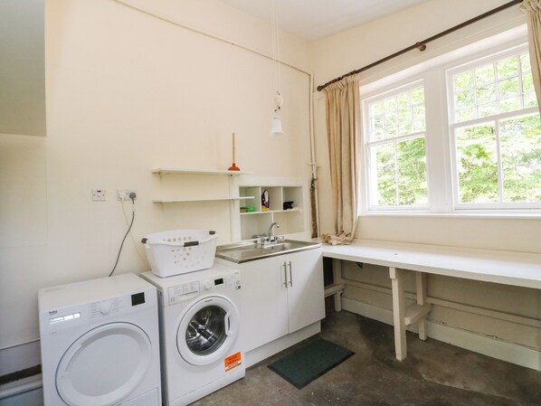 A laundry room with a washing machine, dryer, sink, and a window with curtains.