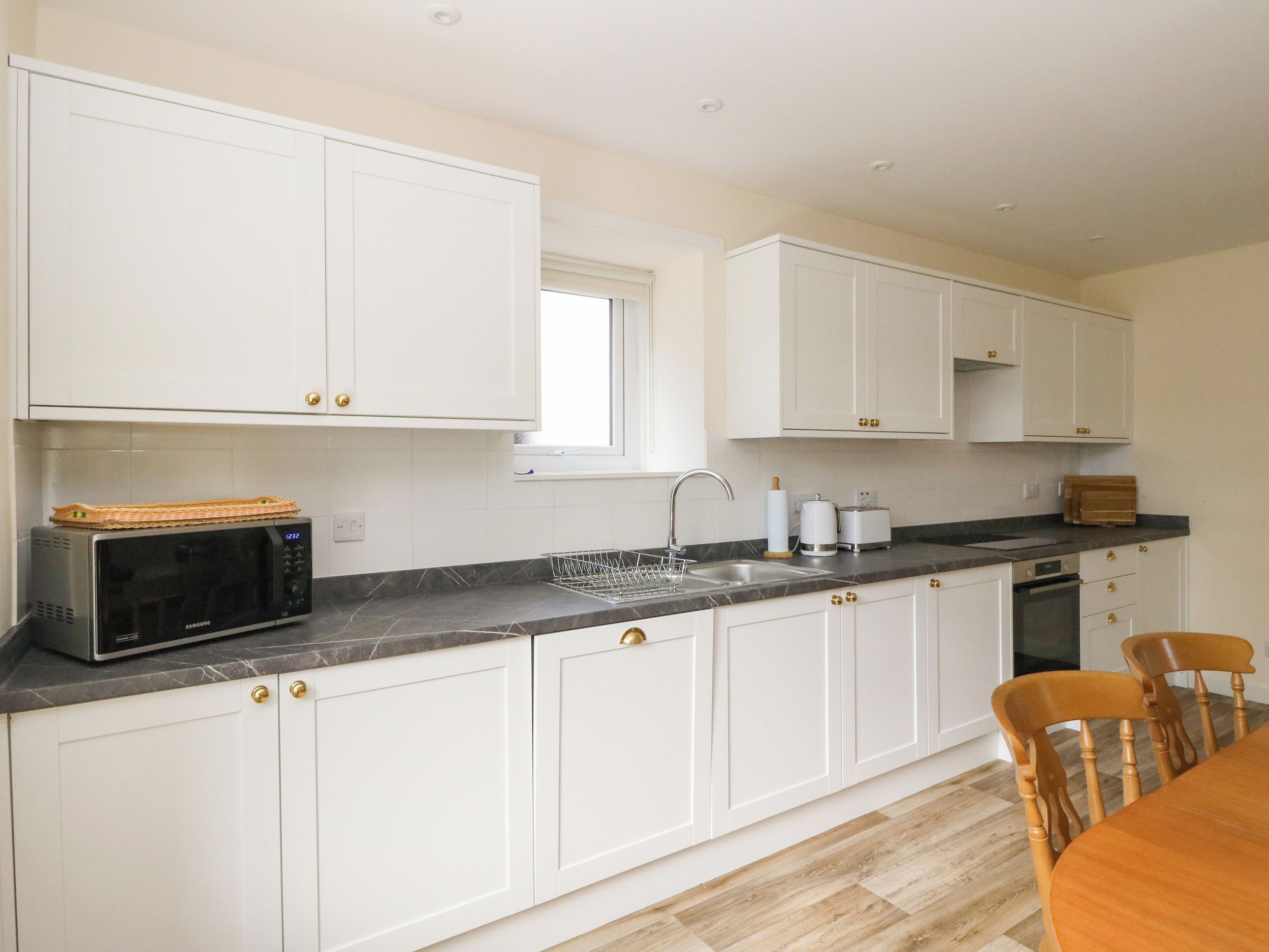 A modern kitchen with white cabinets, a microwave, a sink, and a wooden dining table.