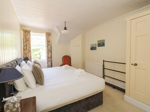A bedroom with a bed, a chair, a bedside table, a lamp, a window with curtains, and a door.