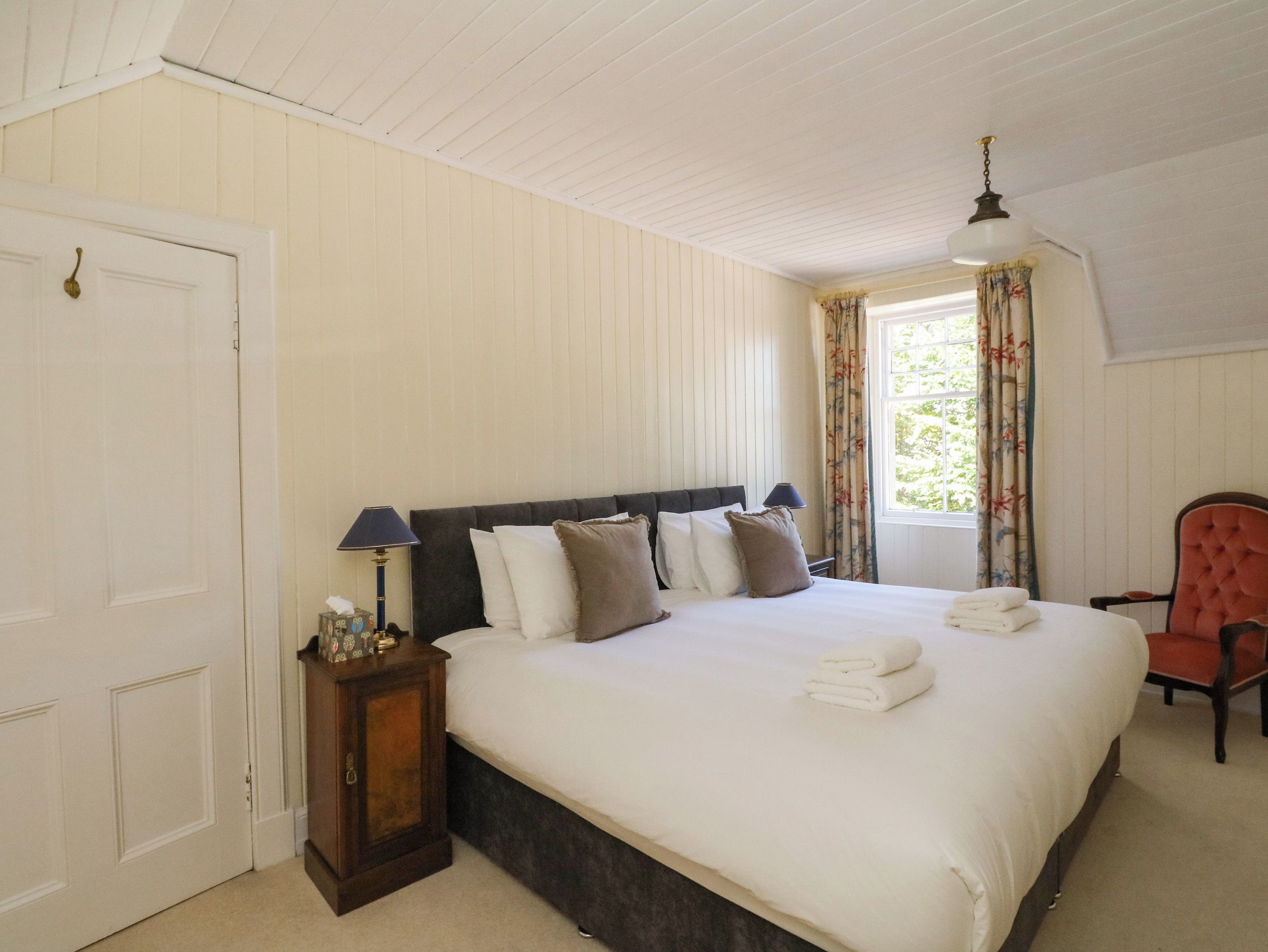 A bedroom with a bed, a nightstand, a chair, a window with curtains, and a door.