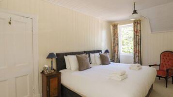 A bedroom with a bed, a nightstand, a chair, a window with curtains, and a door.