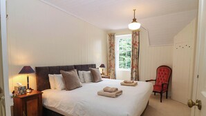 Un dormitorio con una cama grande, dos mesitas de noche, una silla, una ventana con cortinas y una puerta.