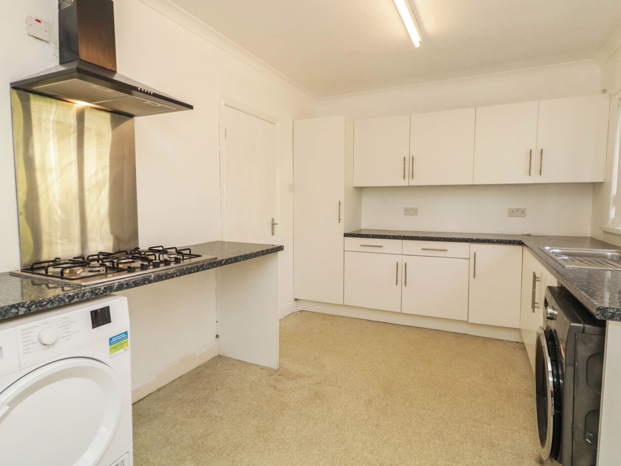 A kitchen with white cabinets, a gas stove, a washing machine, and a dishwasher.