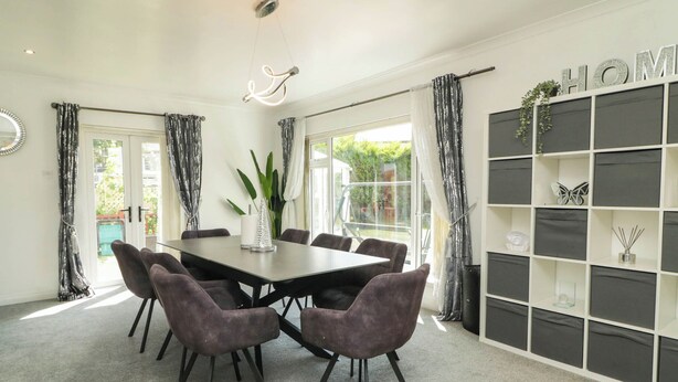 A dining area with a table and chairs, a decorative light fixture, and a bookshelf with various items.