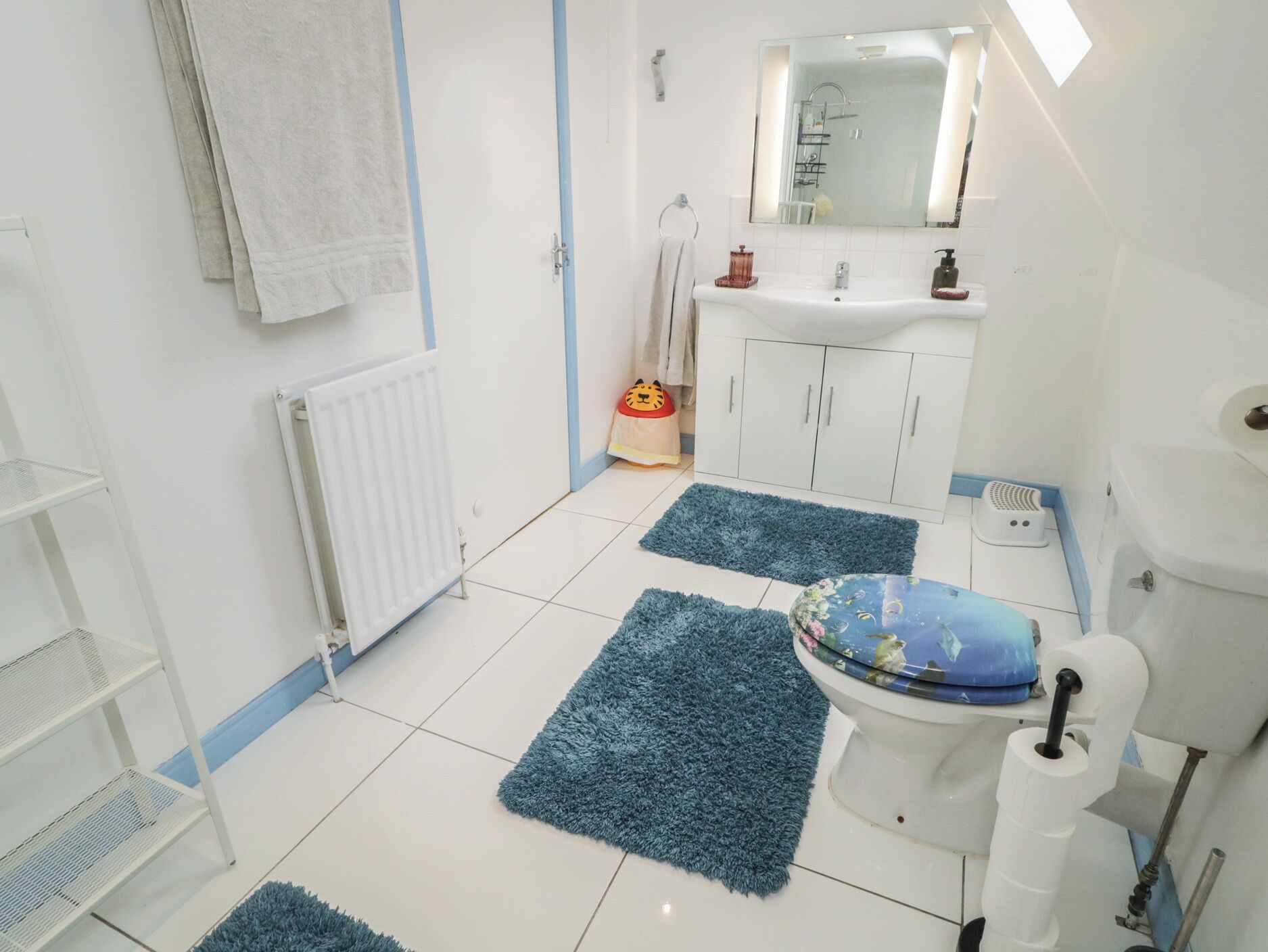 A bathroom with a toilet, sink, mirror, and a radiator. There are blue rugs on the floor.