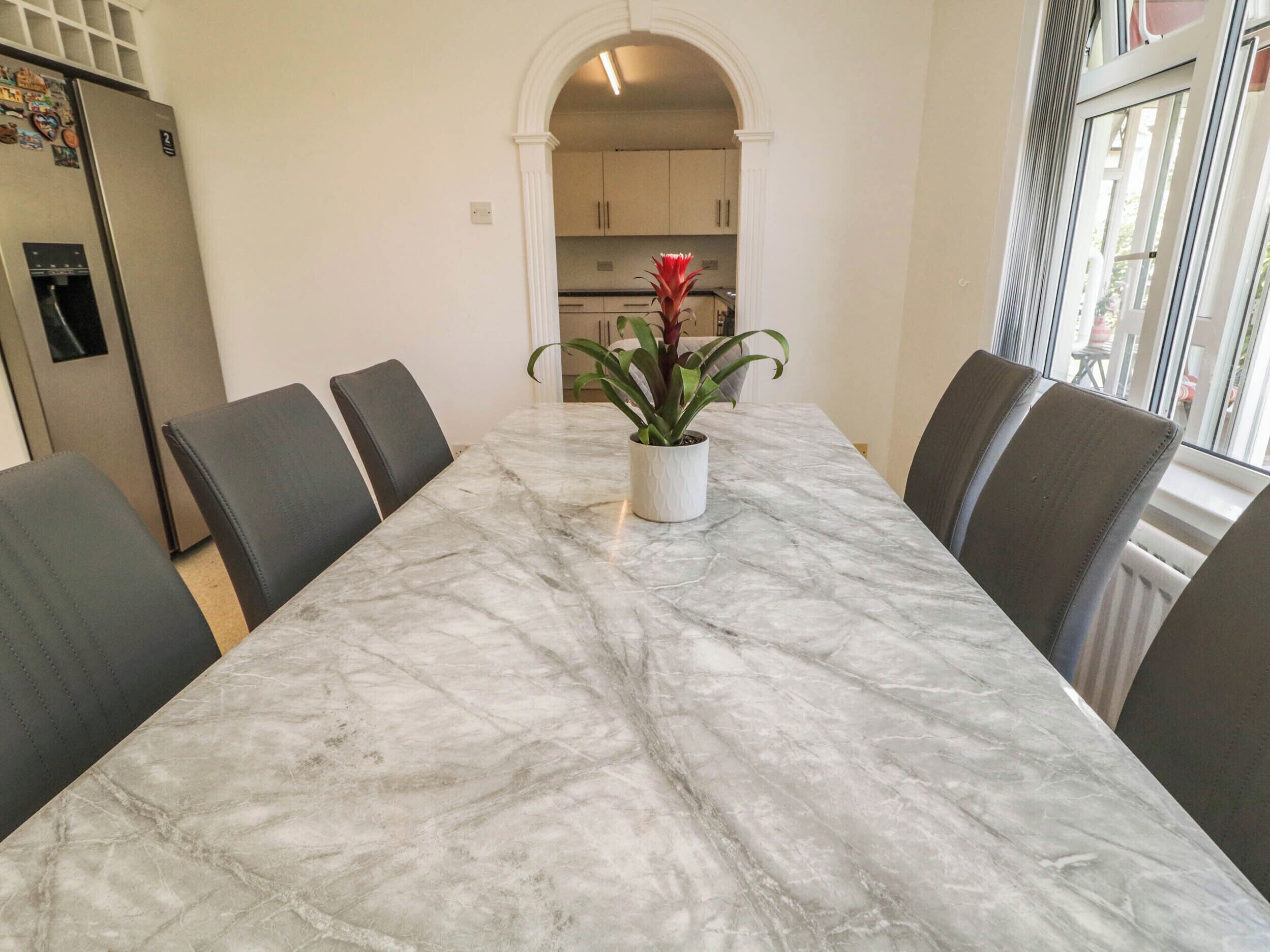 A dining table with six chairs, a potted plant, and a kitchen in the background.