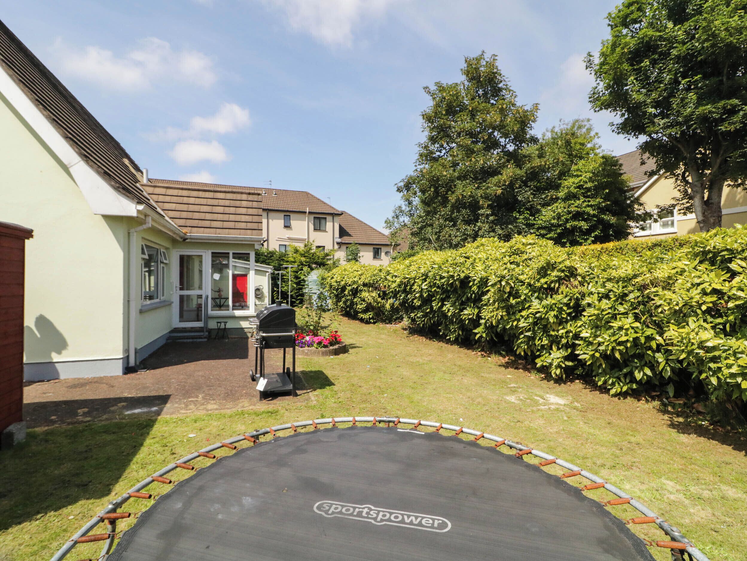 Patio trasero residencial con un trampolín, una parrilla para barbacoa y un seto bien cuidado.