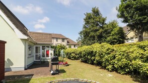 A residential backyard with a trampoline, a barbecue grill, and a well-maintained hedge.