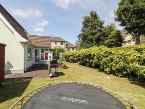 Patio trasero residencial con un trampolín, una parrilla para barbacoa y un seto bien cuidado.