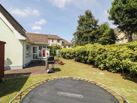Patio trasero residencial con un trampolín, una parrilla para barbacoa y un seto bien cuidado.