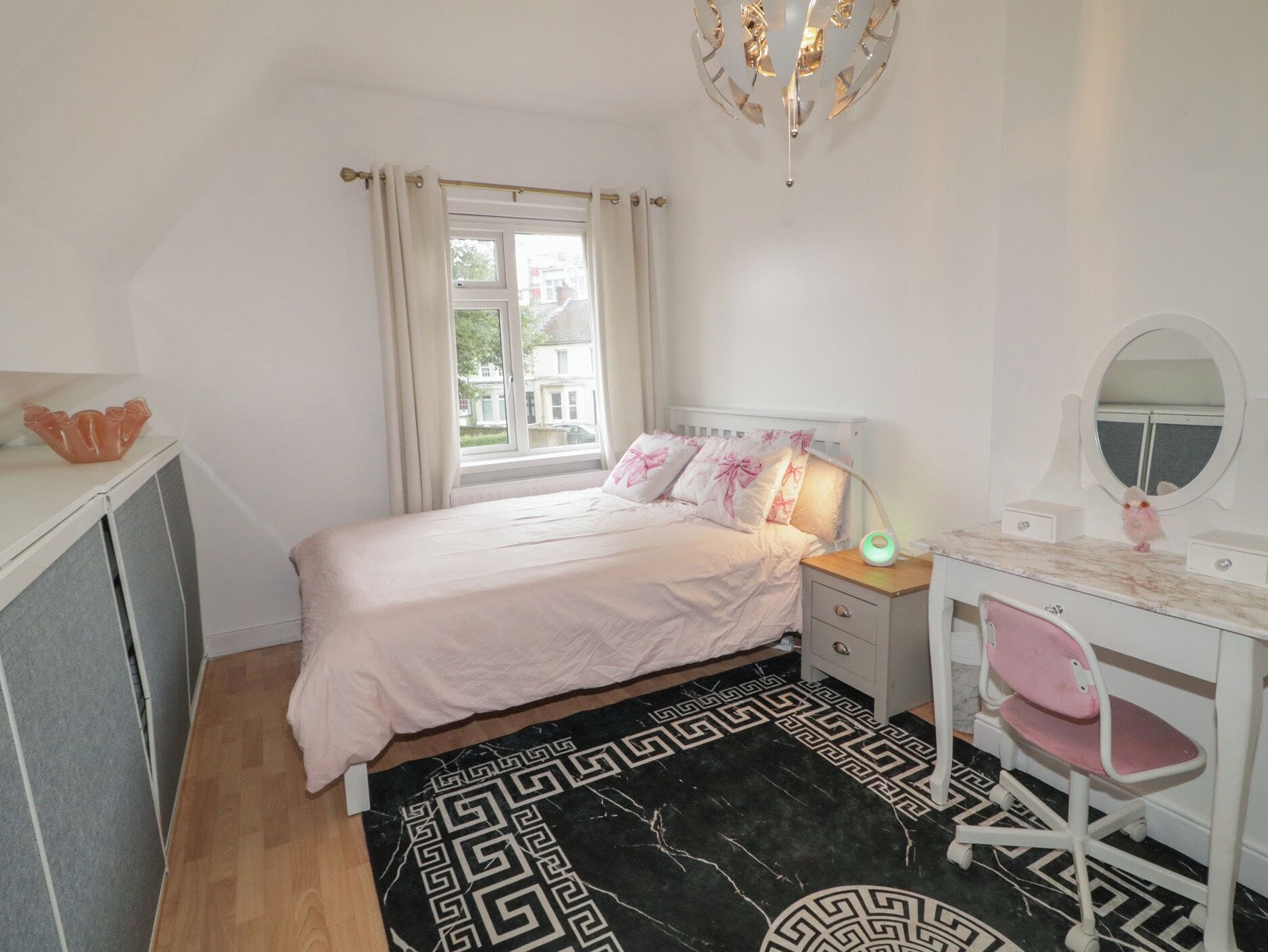 Un dormitorio con cama, mesita de noche, escritorio, silla y una ventana con cortinas.