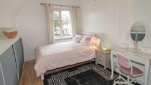 A bedroom with a bed, bedside table, desk, chair, and a window with curtains.