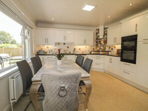A modern kitchen with white cabinets, a marble countertop, and a dining area with a table and chairs.