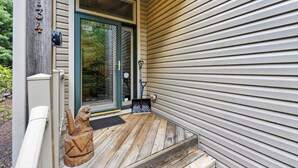 A wooden porch with a metal number plaque, a door with a notice, and a small wooden sculpture. - Luxury Chalet | Hot Tub, Ski Views & Lake Club (Lake Harmony)