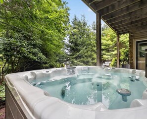 Een hottub in een overdekte buitenruimte, met bomen en een gebouw op de achtergrond.