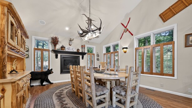 A dining area with a wooden table and chairs, a fireplace, and a bear statue. - Luxury Chalet | Hot Tub, Ski Views & Lake Club (Lake Harmony)