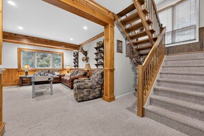 A spacious living area with a wooden staircase, a fireplace, and a large window. - Luxury Chalet | Hot Tub, Ski Views & Lake Club (Lake Harmony)