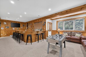 A cozy room with a foosball table, bar area, and seating. - Luxury Chalet | Hot Tub, Ski Views & Lake Club (Lake Harmony)